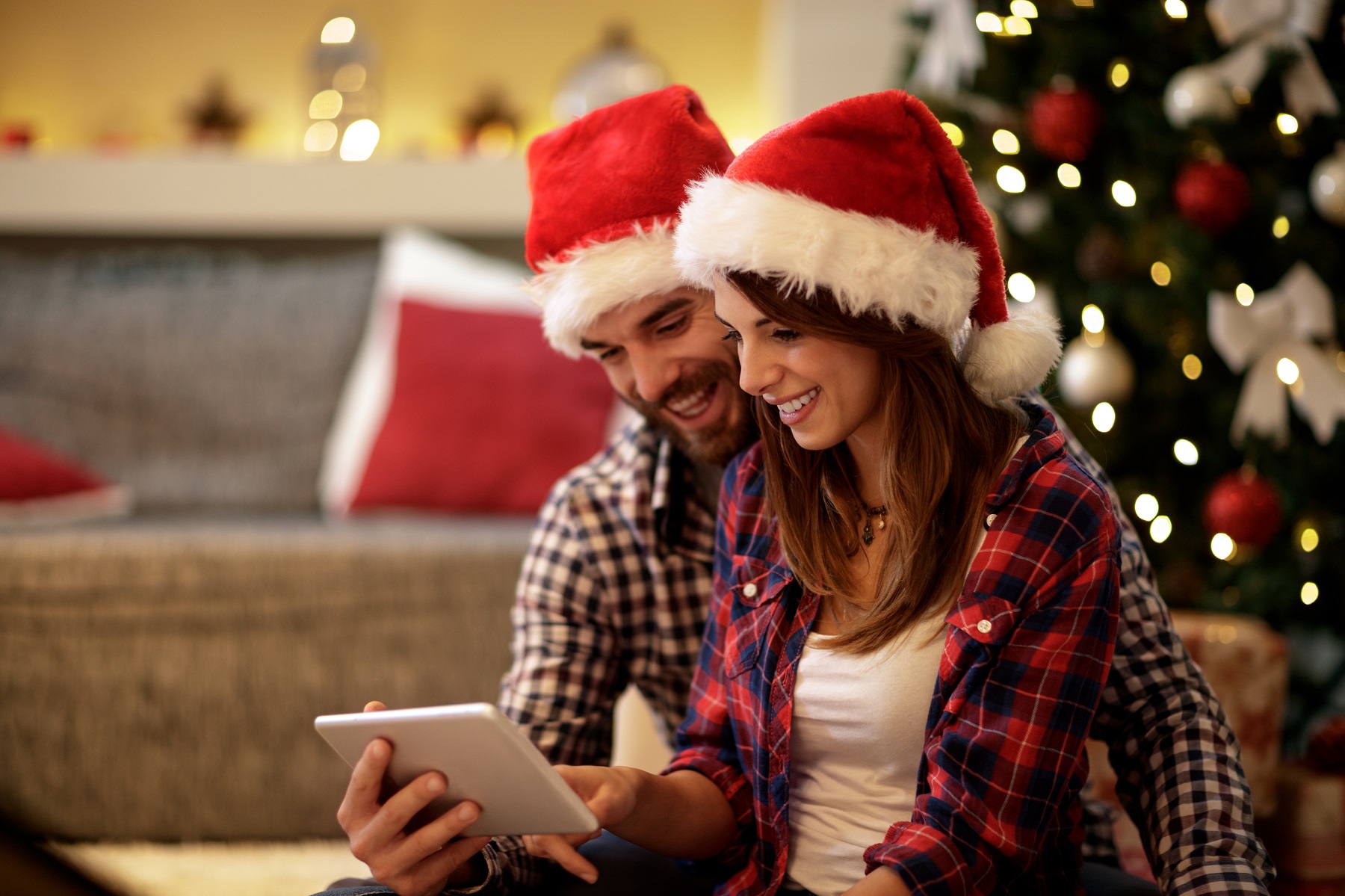 Zwei glückliche Menschen mit Weihnachtsmütze schauen auf einen Bildschirm