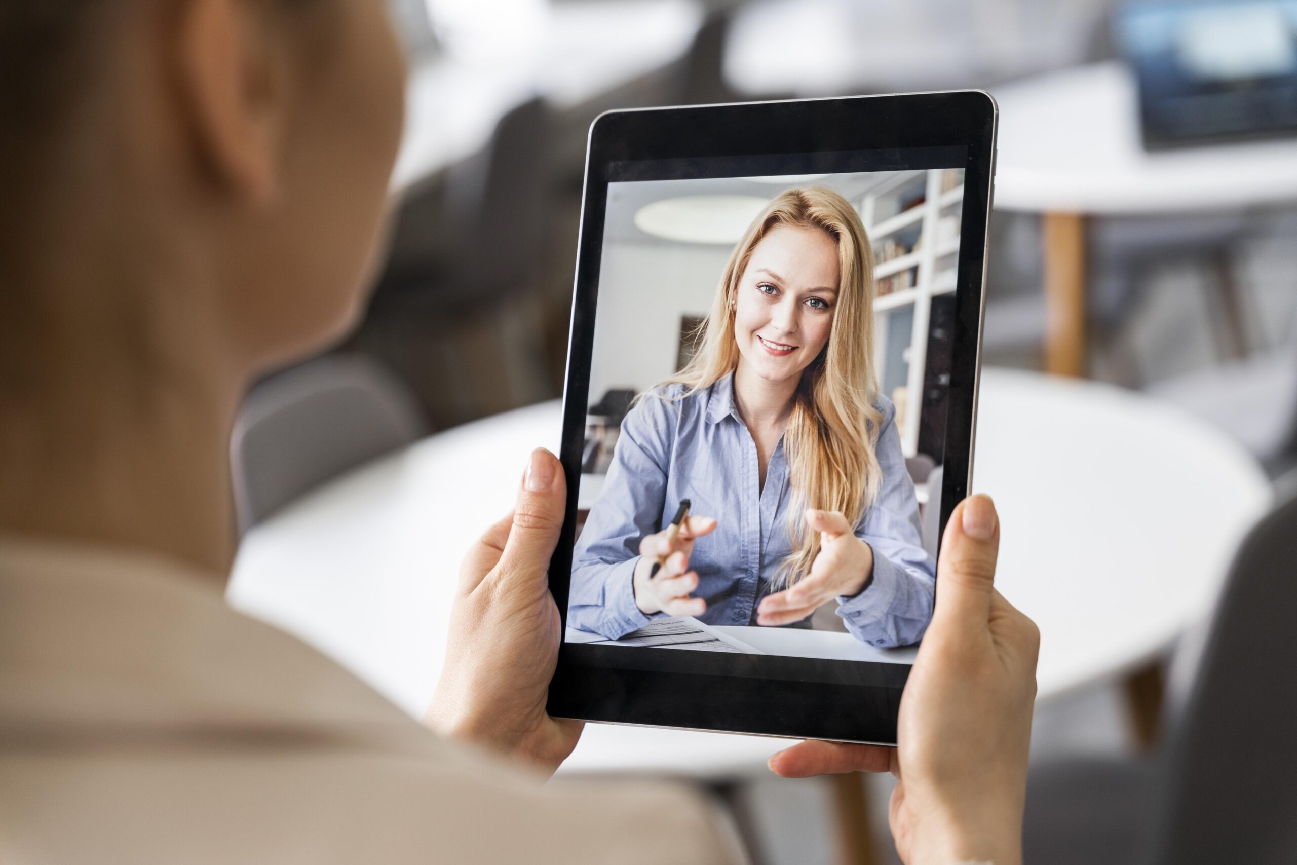 Eine Frau schaut auf ein Tablet, auf dem eine andere Frau zu sehen ist.