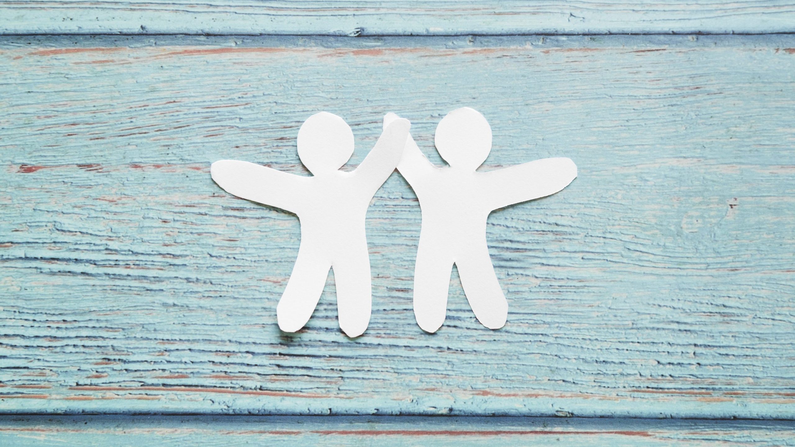 Zwei aus Papier ausgeschnittene Männchen geben sich High-Five