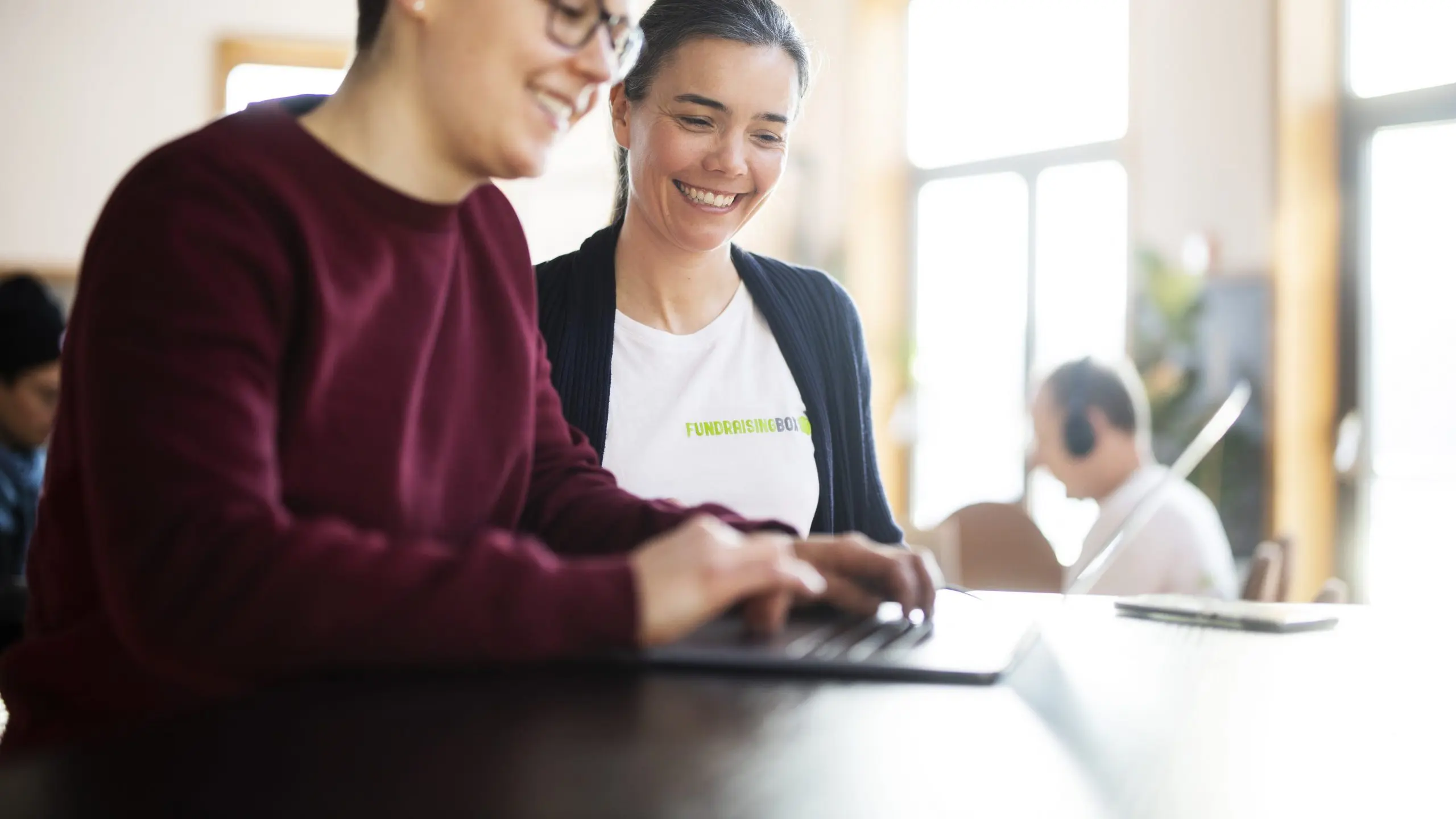 Frau mit FundraisingBox und weitere Frau schauen in Laptop und lächeln