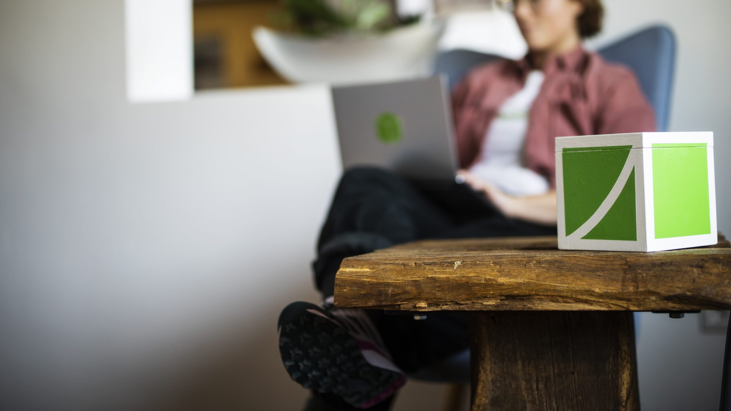 MItarbeiterin der Wikando sitzt mit Laptop auf Sessel, FundraisingBox im Vordergrund auf einem Tisch