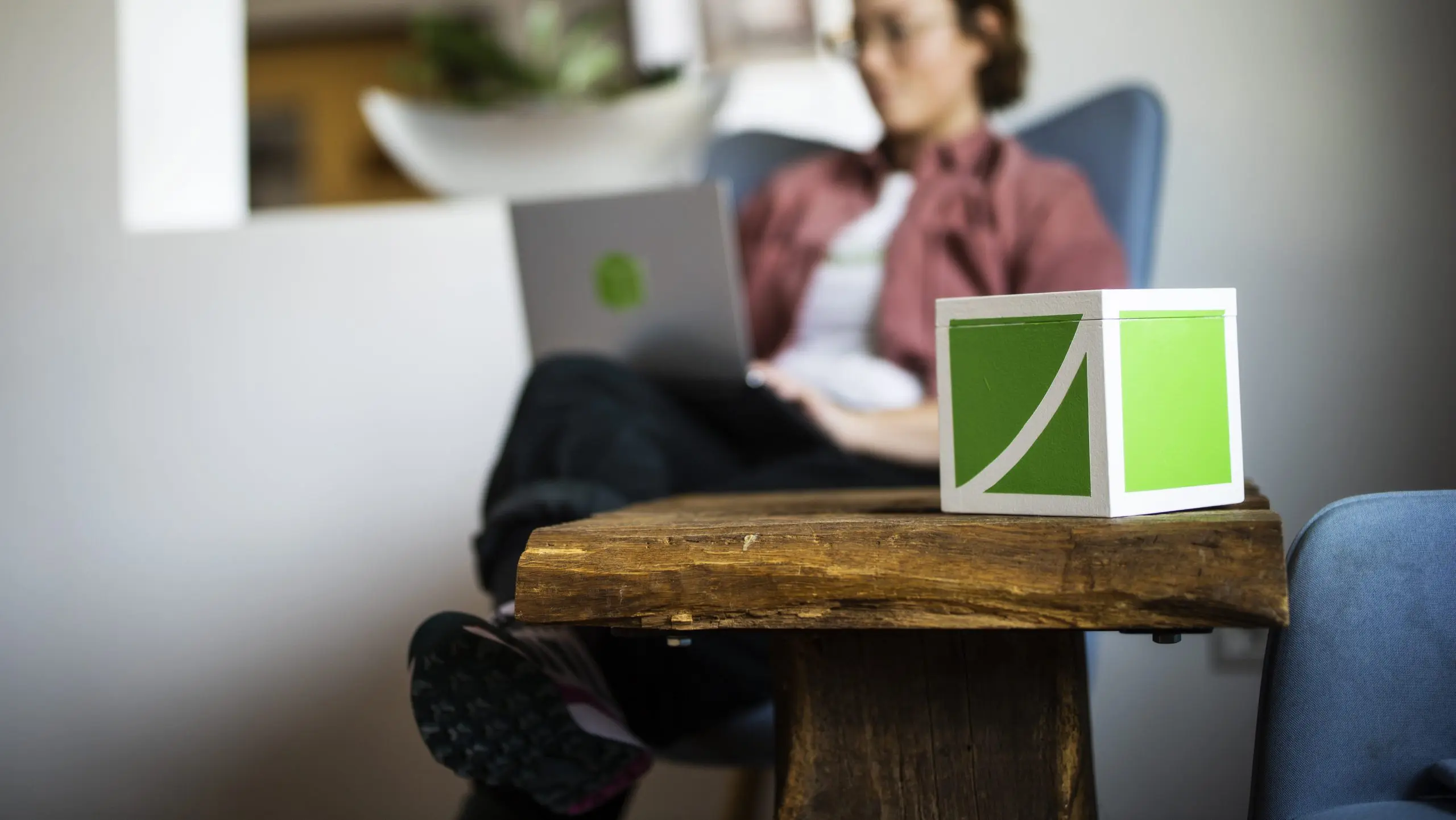 MItarbeiterin der Wikando sitzt mit Laptop auf Sessel, FundraisingBox im Vordergrund auf einem Tisch