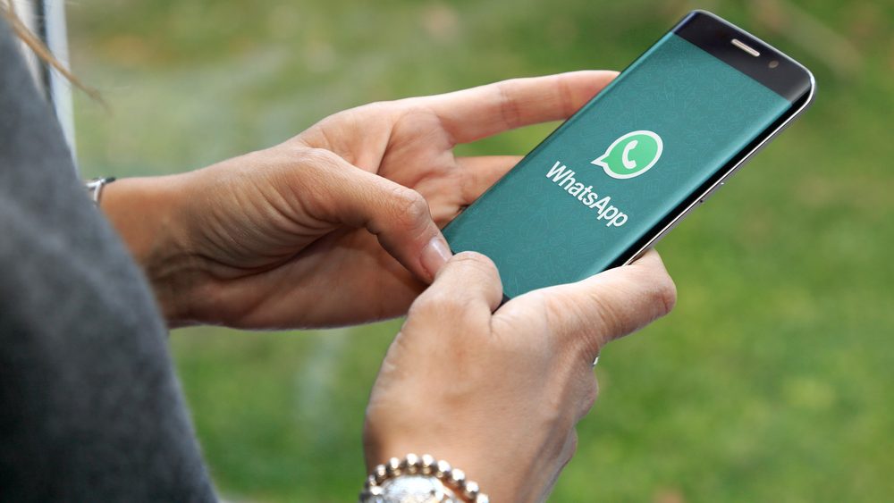 Person hält ein Mobiltelefon, auf dem das WhatsApp-Logo zu sehen ist