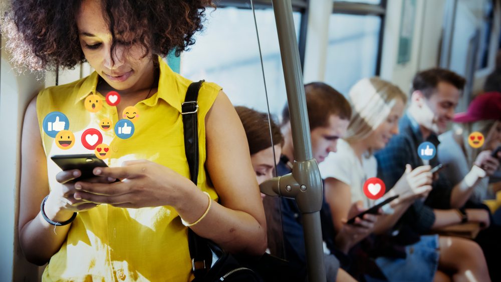Social Media Symbole über Mobiltelefonen von Menschen in einer U-Bahn.