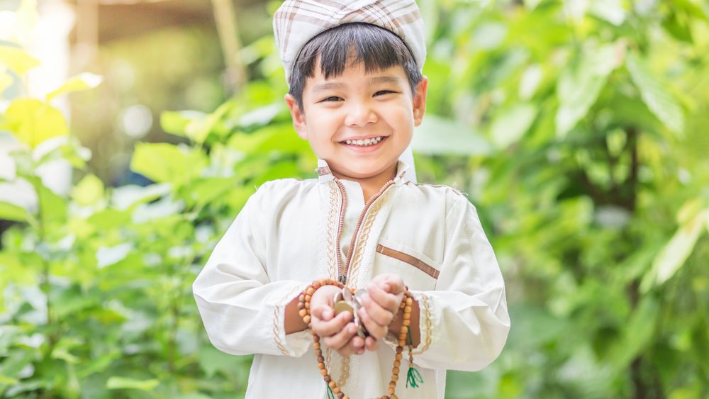 Ein lachendes muslimisches Kind hält Münzen als Spende zu Ramadan in den Händen